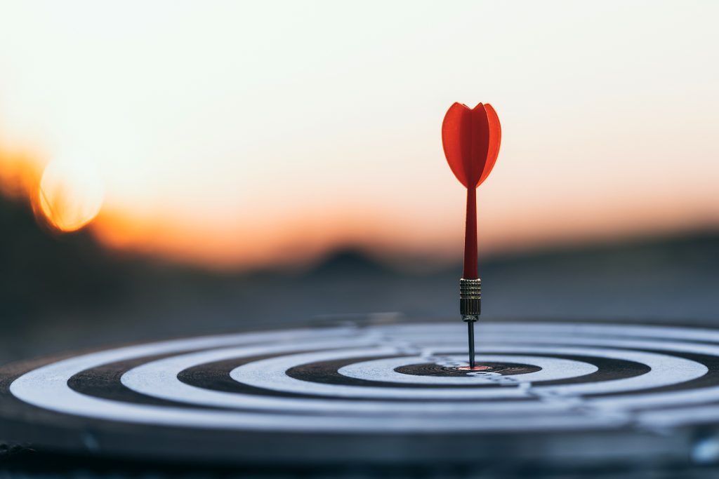 Close up red dart arrow hitting target center dartboard on sunse